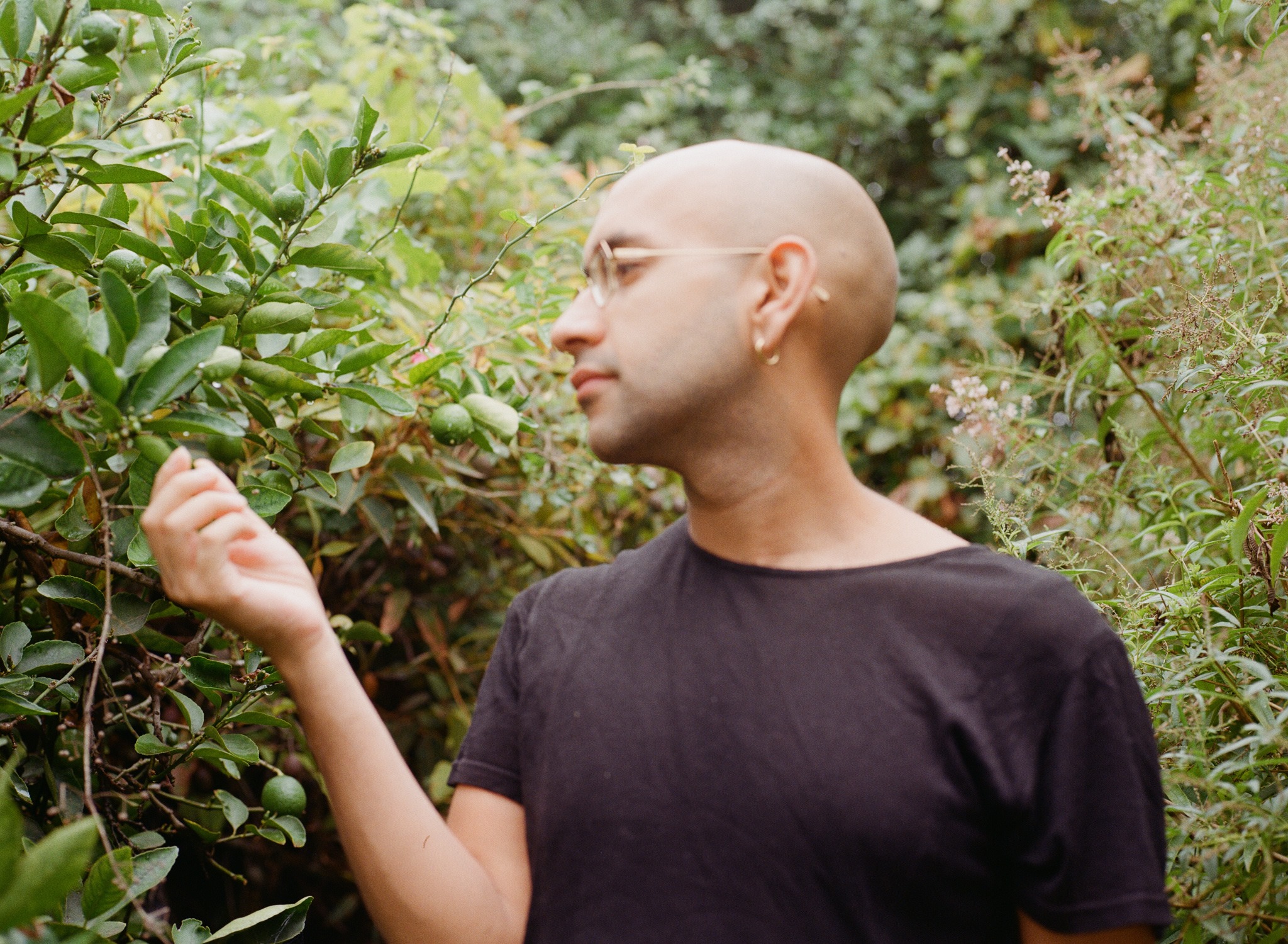 a person with glasses and with an earring looking sideways to surrounded by trees