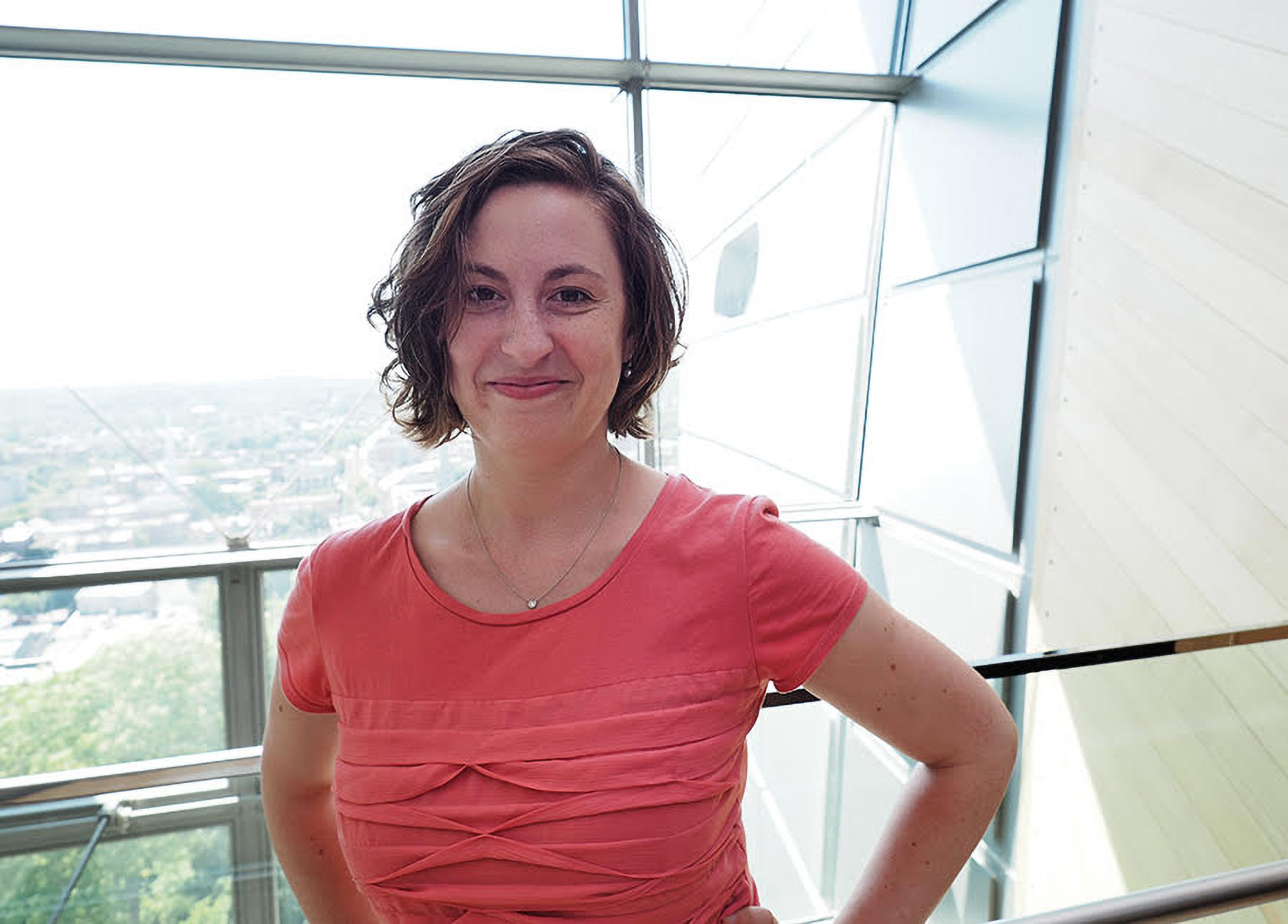 a woman in red standing in front of a big window.