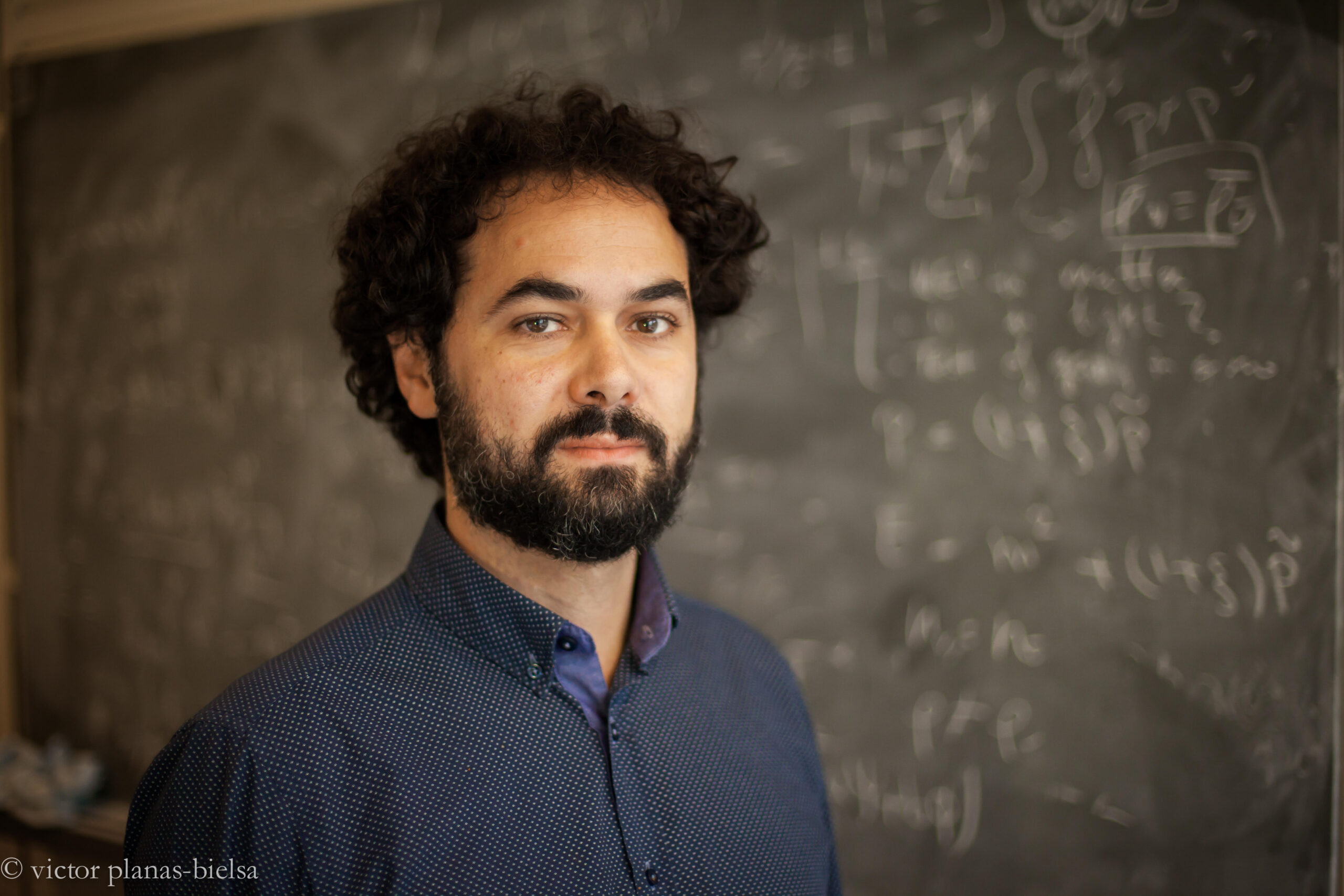 a man with beard in front of a blackboard