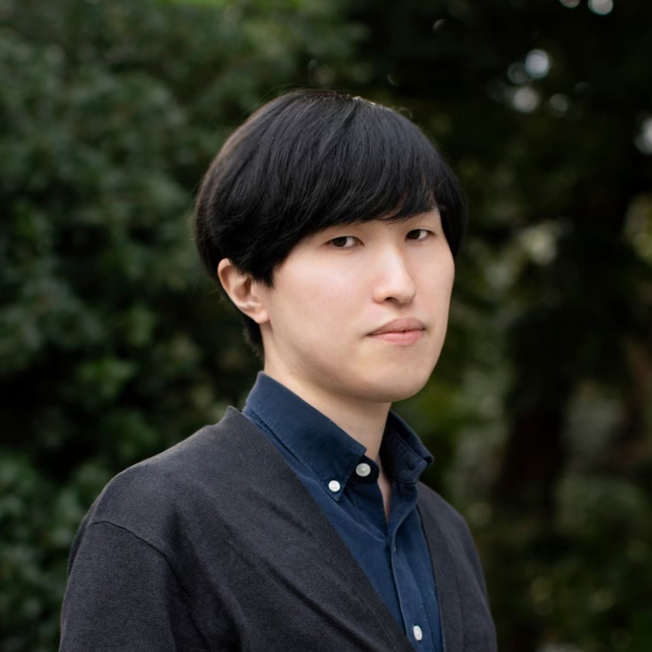 a man with short black hair looking sideways at the camera in front of a green background