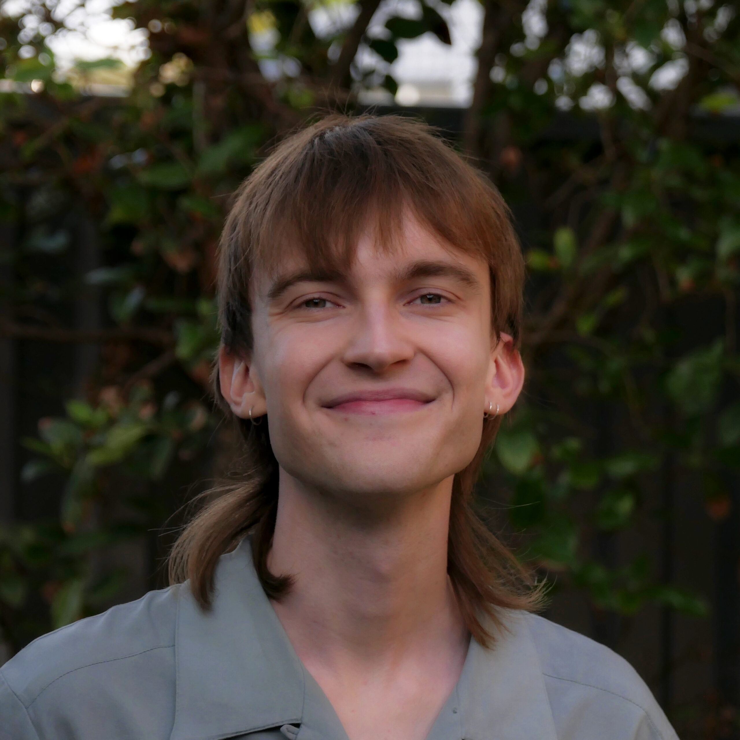 A square photo of the artist looking right into the camera. She wears a warm smile and a green collared shirt.