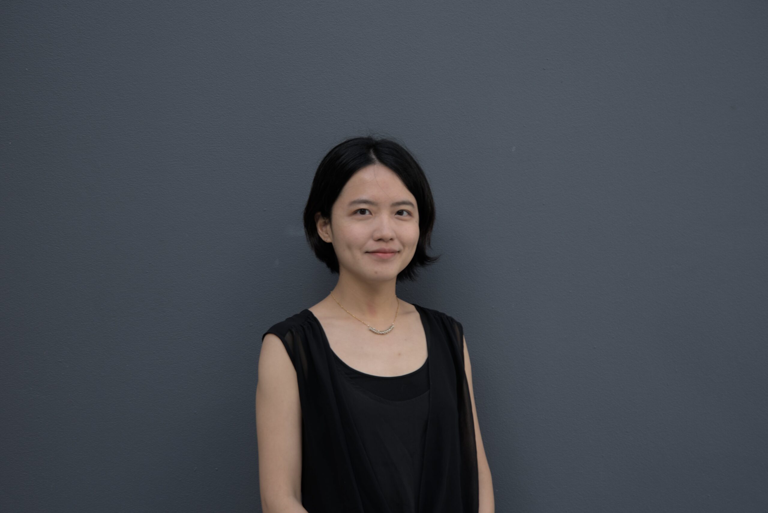 This image is of a woman wearing a black shirt standing in front of a grey wall.