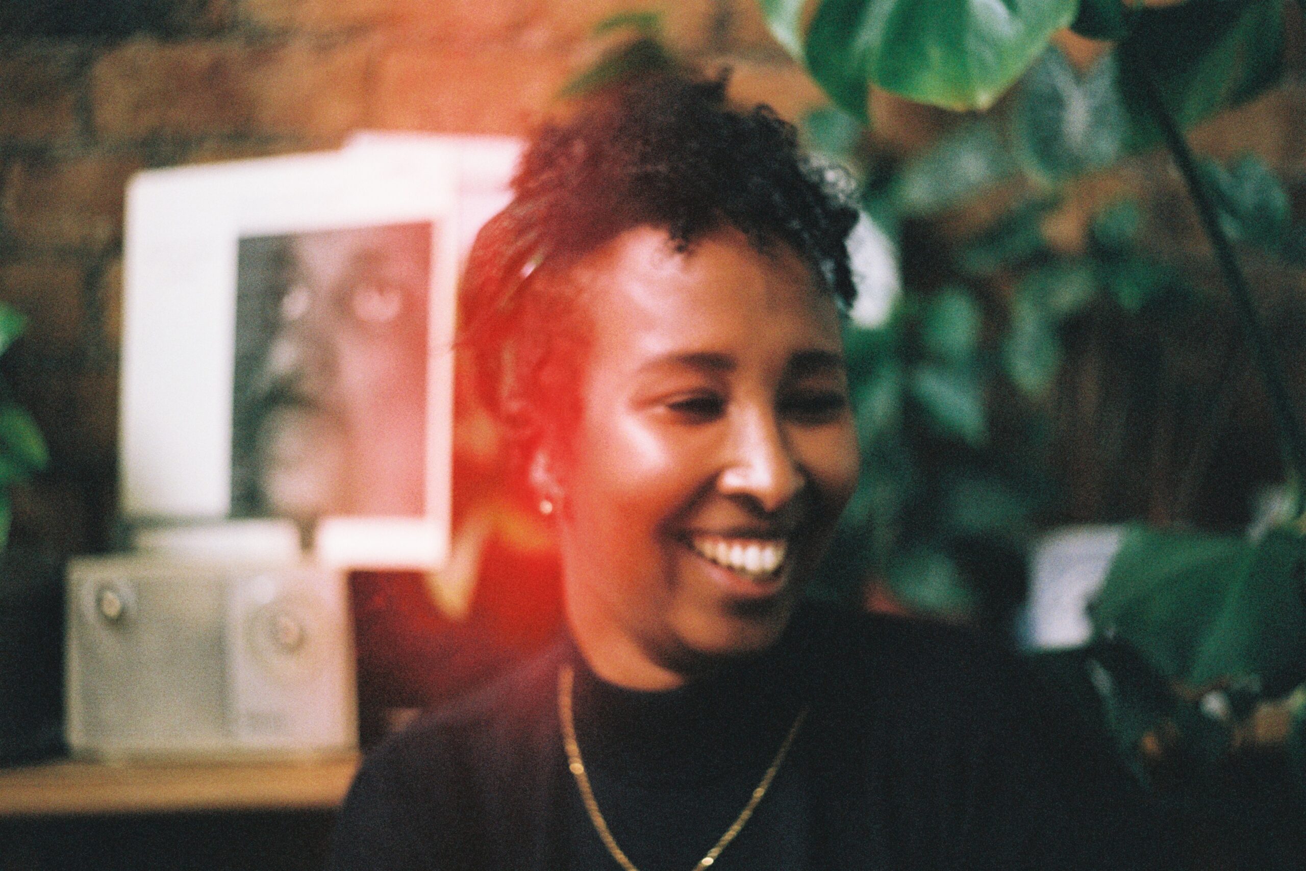 A woman with curly black hair and wearing a black turtleneck and is smiling looking away from the camera