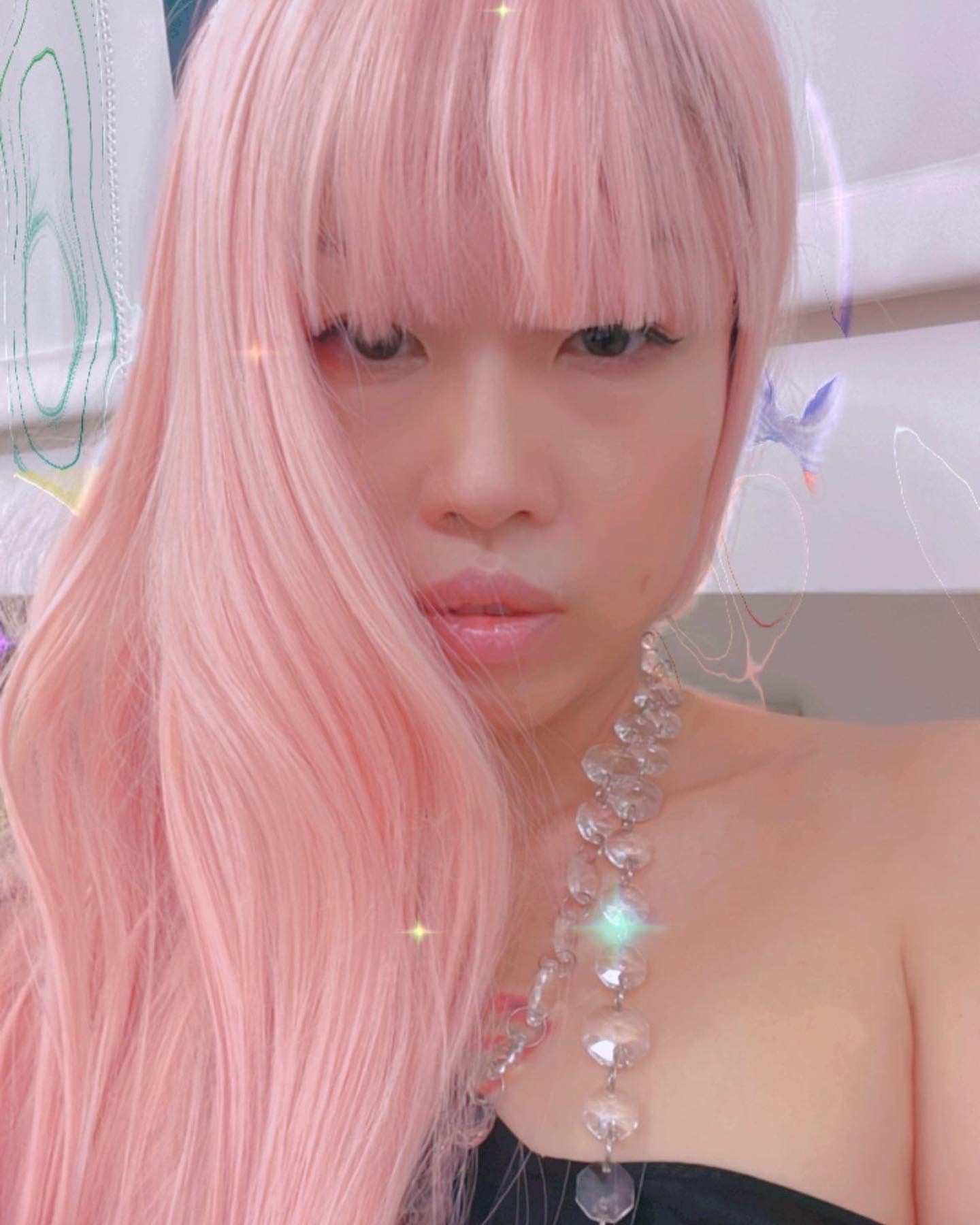 Portrait of a woman with bright pink long hair staring directly at the camera. She wears a bubbly necklace.