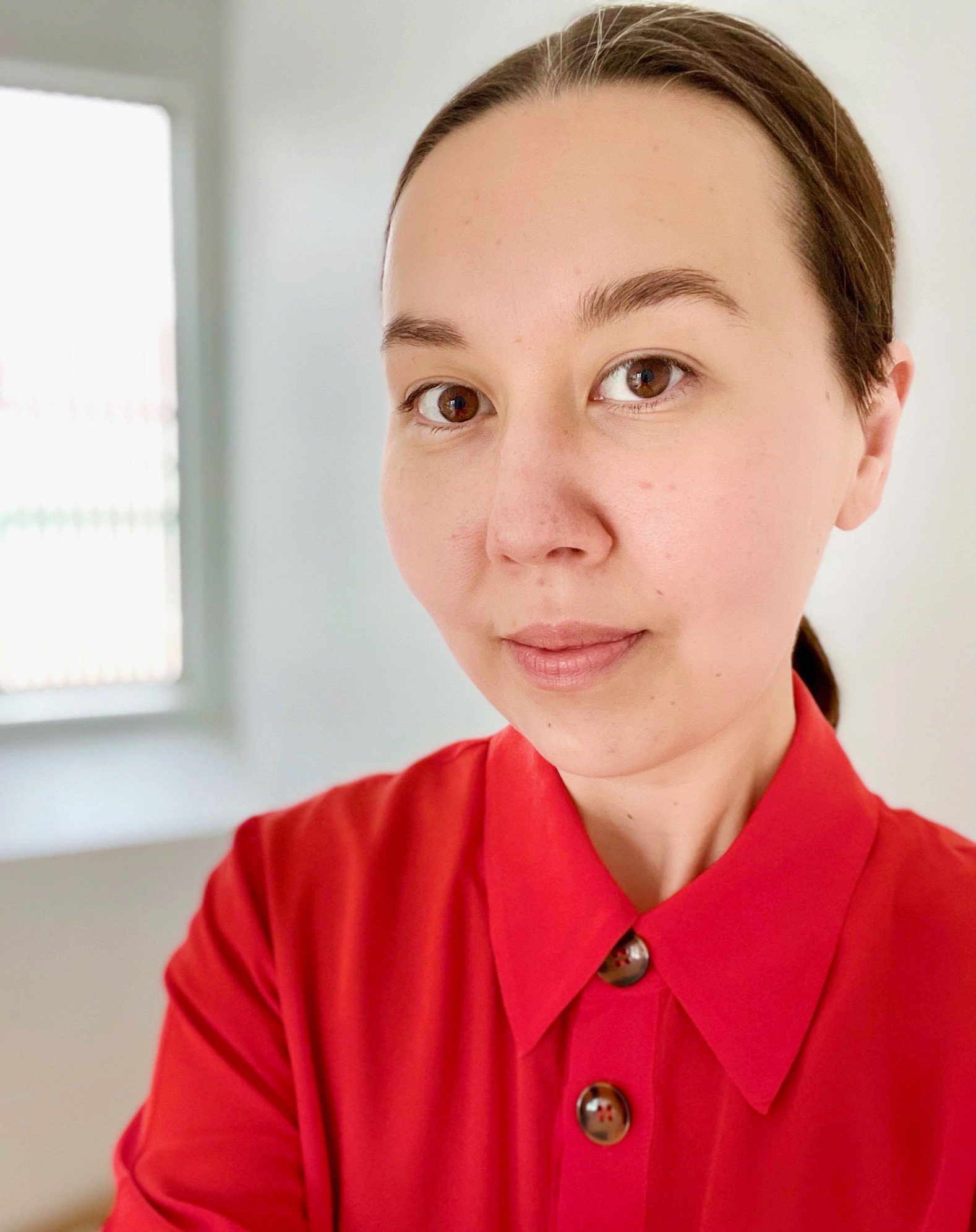 a woman with a bright red short looking straight at the camera with her hair pulled tightly back