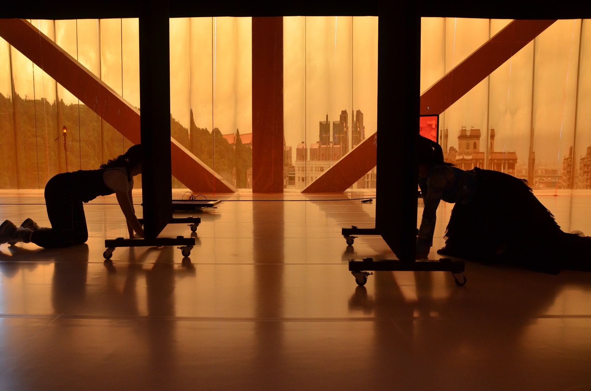 This image is of two women pushing the mirrors with their heads and crawling towards each other in a room with orange filters.