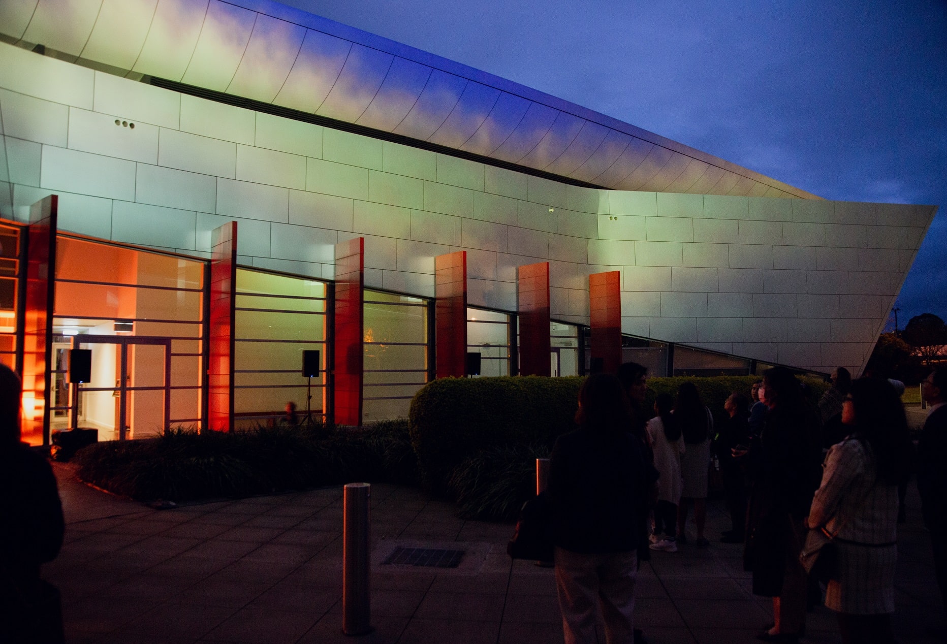 The Campbelltown Arts Centre building with sharp archictectural lines and a rectuacular screen like panel has imagery of the a dark setting sky and fluffy clouds projected onto it, with the dark setting sky the backdrop to the building.