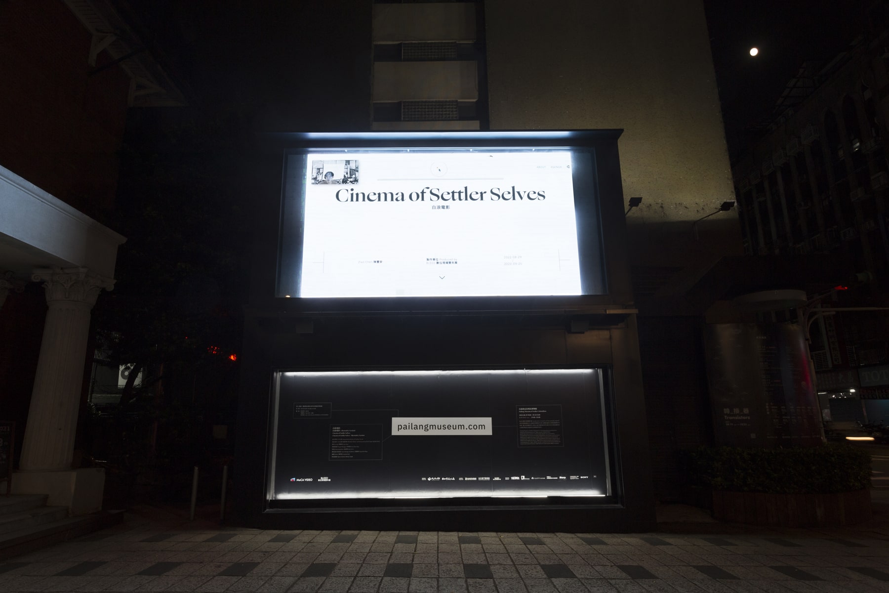 At night, In front of the plaza in downtown Taipei, a giant LED screen is playing a video artwork by Taiwanese artist Wu Chi-Yu’ video artwork titled “Cinema of Settler Selves” displayed on the screen with black characters on a white background.